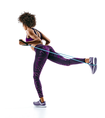 Sporty girl doing exercises with resistance band isolated on white background. Back view. Strength and motivation.の写真素材