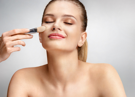 Beautiful woman applying liquid foundation on her face on grey backgroundの写真素材