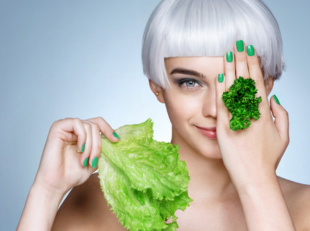 Beautiful blonde girl with parsley and lettuce leaves in her hand. Photo of fashion blonde girl on blue background. Healthy lifestyle conceptの写真素材
