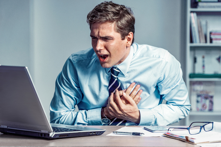 Office manager having heart attack. Photo of young man holding hand on painful chest in the workplace. Medical concept.の写真素材