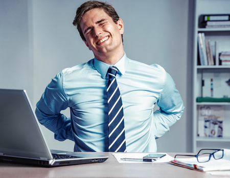 Employee suffers from severe pain in back. Photo of man working in the office. Medical concept.の写真素材