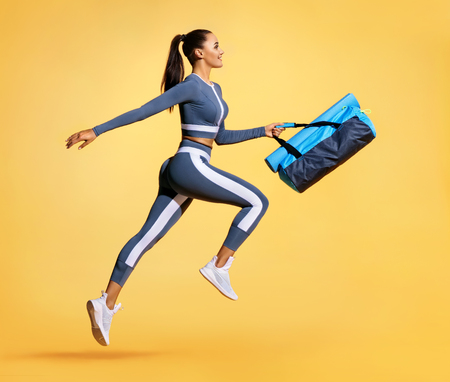 Go to training. Sporty woman with bag running in silhouette on yellow background. Dynamic movement. Side view. Sports and healthy lifestyleの写真素材