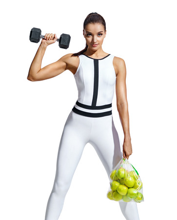Strong woman with dumbbell and bag of apples. Photo of muscular woman in fashionable sportswear on white background. Healthy lifestyle and motivationの写真素材