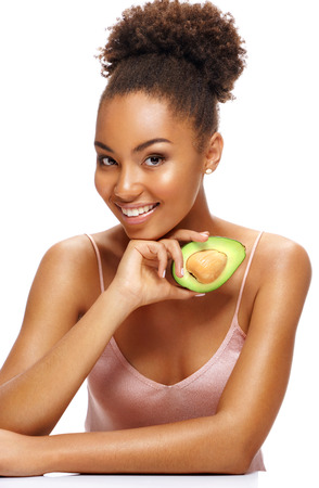 Beautiful healthy girl with half an avocado. Photo of african american girl on white background. Beauty & Skin care conceptの写真素材