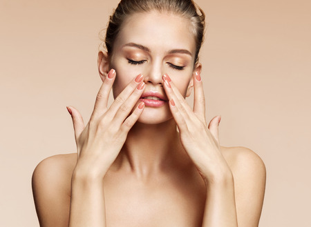 Beautiful woman doing facial massage, touching her face. Photo of woman with clean healthy skin on beige background. Skin care and beauty conceptの写真素材