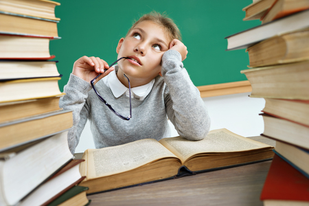 Dreamy school girl, looking up. Photo of little girl with open book, daydreaming or thinking of something. Education conceptの写真素材