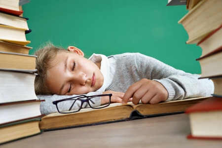 Tired schoolgirl sleeping on book. Photo of little girl in school around books. Education conceptの写真素材