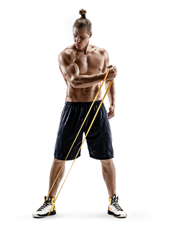 Young strong man with naked torso performs exercises using resistance band. Photo of muscular man isolated on white background. Strength and motivation. Full lengthの写真素材