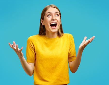 Happy girl gestures actively from happiness. Photo of attractive girl in yellow sweater on blue background. Emotions and pleasant feelings concept.の写真素材