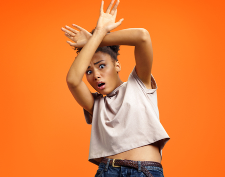 Scared girl outstretched her palms, hiding her face. Photo of african american girl wears casual outfit on orange background. Emotions and feelings concept.の写真素材