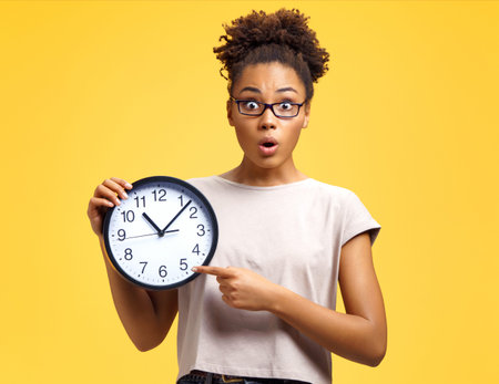 Time to work! Student with shocked face holds clock and points to them. Photo of african american...