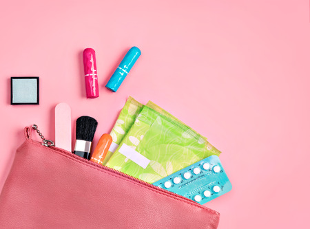 Lady's bag. Sanitary pads and tampons in cosmetic bag on pink background. Concept of critical days, menstruationの写真素材