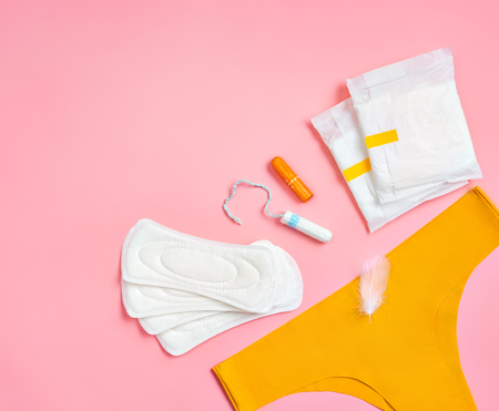 Yellow pants with sanitary napkins and tampons on pink background. Concept of critical days, menstruationの写真素材