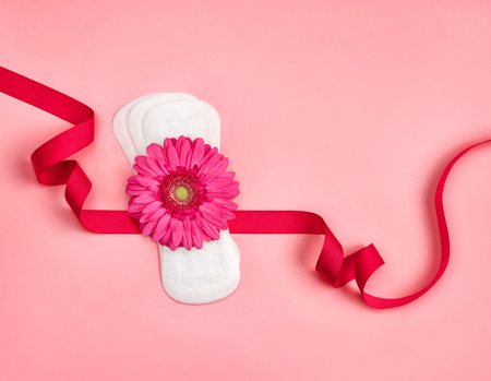 Daily sanitary napkins with gerbera flower on pink background. Concept of critical days, menstruationの写真素材