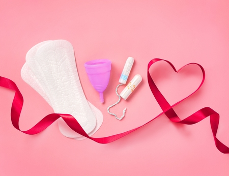Sanitary napkins, tampon and menstrual cup with red ribbon on pink background. Concept of critical days, menstruationの写真素材
