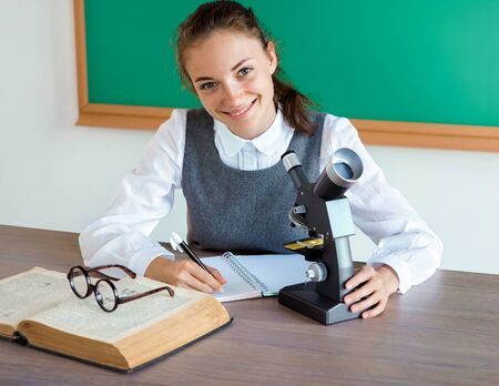 Smiling student doing research using microscope. Photo of girl in uniform, wearing glasses. Education conceptの写真素材