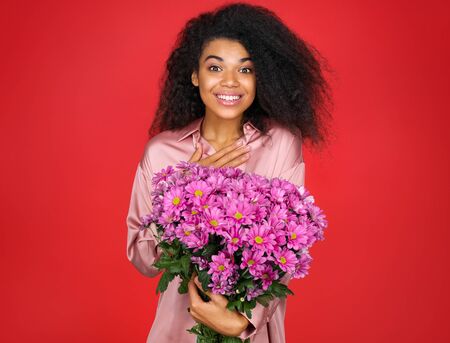 Happy girl with spring flowers bouquet. Photo of young girl on red backgroundの写真素材