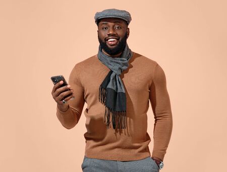 Handsome man using smartphone. Photo of african man in stylish casual clothes on beige background.の写真素材