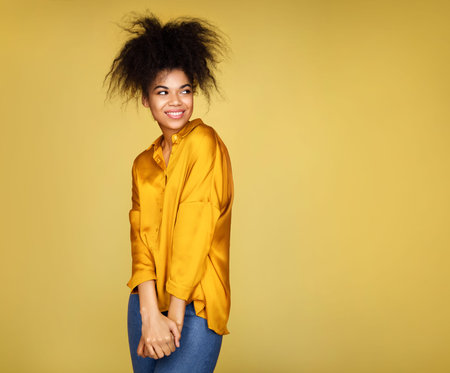 Attractive shy girl, looking aside. Photo of african american girl on yellow background