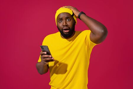 Stunned man receives message reminder on smart phone, forgets about something, on red backgroundの写真素材