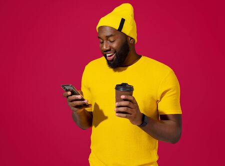 Handsome man uses the phone and drinks coffee, checks for new message on red backgroundの写真素材
