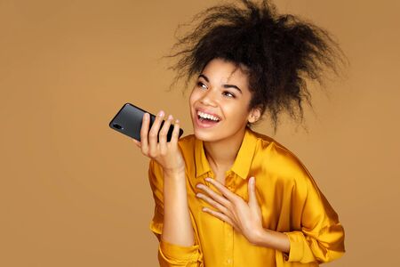 Girl uses the phone, leaves a voice message. Photo of african american girl on beige backgroundの写真素材
