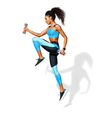 Sporty girl jumping with dumbbells. Photo of african american girl in fashionable sportswear on white background. Dynamic movement. Side view. Full length. Sports and healthy lifestyleの写真素材