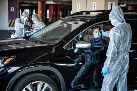 Medical worker measuring temperature of woman through car window before leaving quarantine zone. Stay at homeの写真素材