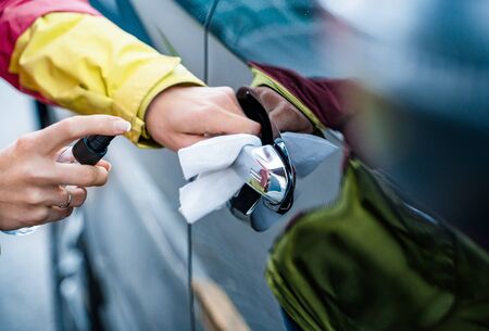 Hand of woman is spraying disinfectant spray on handle of car door, wipe clean surfaces that are frequently touchedの写真素材