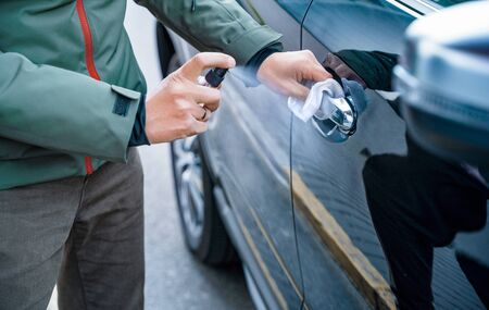 Hand of man is spraying disinfectant spray on handle of car door, wipe clean surfaces that are frequently touchedの写真素材