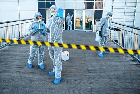 Healthcare worker showing stop gesture. Team of healthcare workers wearing hazmat suits working together to control an outbreak in the cityの写真素材