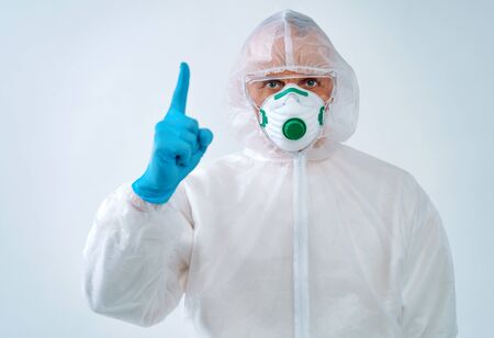 Healthcare worker in protective suit and medical mask pointing finger up. Health care concept.の写真素材