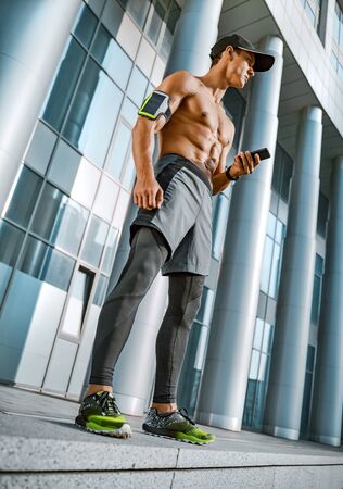Man looking at his phone while exercising. City workout with smart gadgets and sport applicationsの写真素材