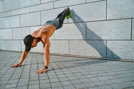 Strong man does push-ups from the wall with his legs up. Photo of young man workout along outdoor in the cityの写真素材