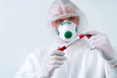 Positive COVID-19 test. Virologist in a medical mask and protective suit holds a test tube with positive blood sampleの写真素材