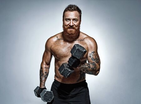 Strong man doing exercises with dumbbell. Photo of man with naked torso on grey background. Strength and motivationの写真素材
