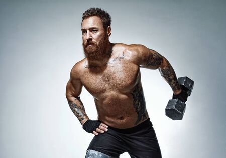 Muscular man doing exercise with heavy weight dumbbells. Photo of man with naked torso on grey background. Strength and motivationの写真素材