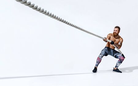 Strong man pulling rope. Photo of sporty man on white background. Strength and motivation. Side view. Full lengthの写真素材