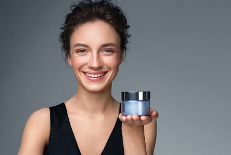 Woman holds jar with cosmetic cream. Photo of attractive woman with perfect makeup on gray background. Beauty conceptの写真素材