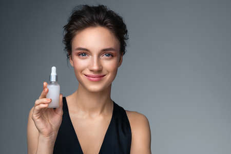Woman holds hyaluronic serum. Photo of attractive woman with perfect makeup on gray background. Beauty conceptの写真素材
