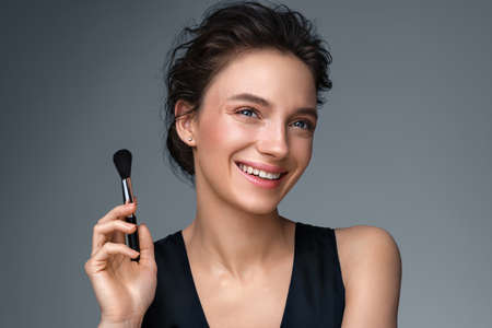 Woman with makeup brush. Photo of woman with perfect makeup on gray background. Beauty conceptの写真素材
