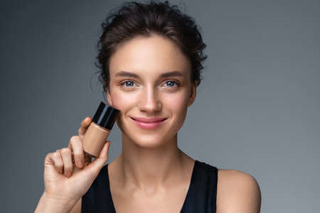 Woman with liquid foundation. Photo of woman with perfect makeup on gray background. Beauty conceptの写真素材