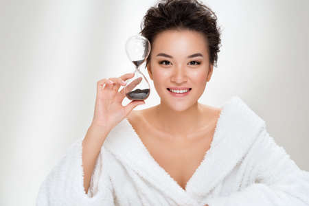 Woman holds hourglass. Photo of asian woman with perfect makeup on white background. Beauty and skin care conceptの写真素材