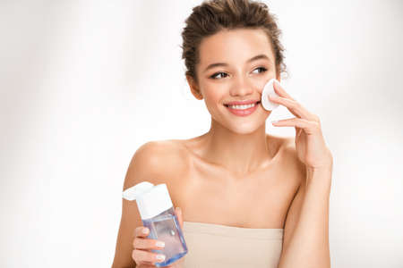 Woman removing makeup, holds cotton pads near face. Photo of woman with perfect skin on white background. Beauty and skin care conceptの写真素材