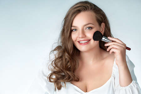 Woman with makeup brush. Photo of woman with perfect makeup on light blue background. Beauty and Skin care concept. Plus size model.の写真素材