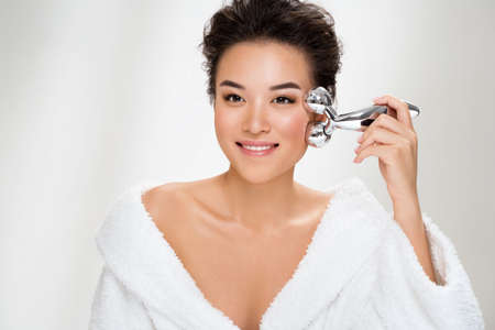 Attractive woman massaging her cheek with massage Y-shaped ball roller on light blue background. Beauty and Skin care concept. Plus size modelの写真素材