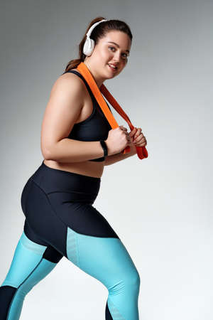Strong girl working with resistance band. Photo of model with curvy figure in fashionable sportswear on gray background. Sports motivation and healthy lifestyleの写真素材