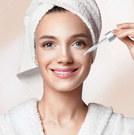 Woman applying hyaluronic serum on her face with pipette. Photo of woman with perfect skin on beige background. Beauty and skin care conceptの写真素材