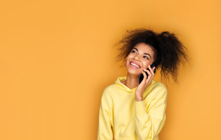 Girl is talking on the phone and smiling. Photo of african american girl on yellow background