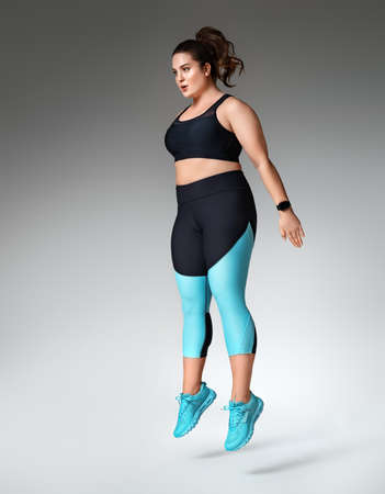 Sporty woman doing jump after exercise squats. Photo of model with curvy figure in fashionable sportswear on gray background. Sports motivation and healthy lifestyleの写真素材